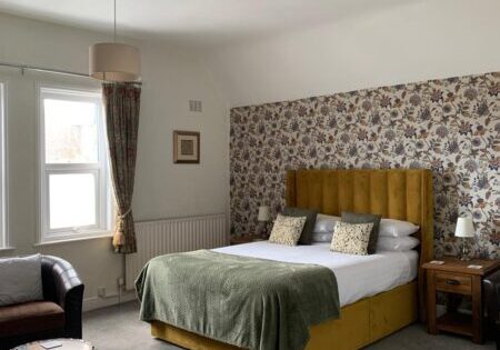 Super-king bedroom with mustard headboard and floral wallpaper